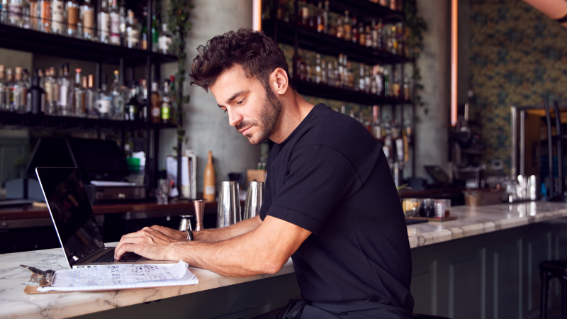 An Image Of A Man Using His Laptop In A Bar.png